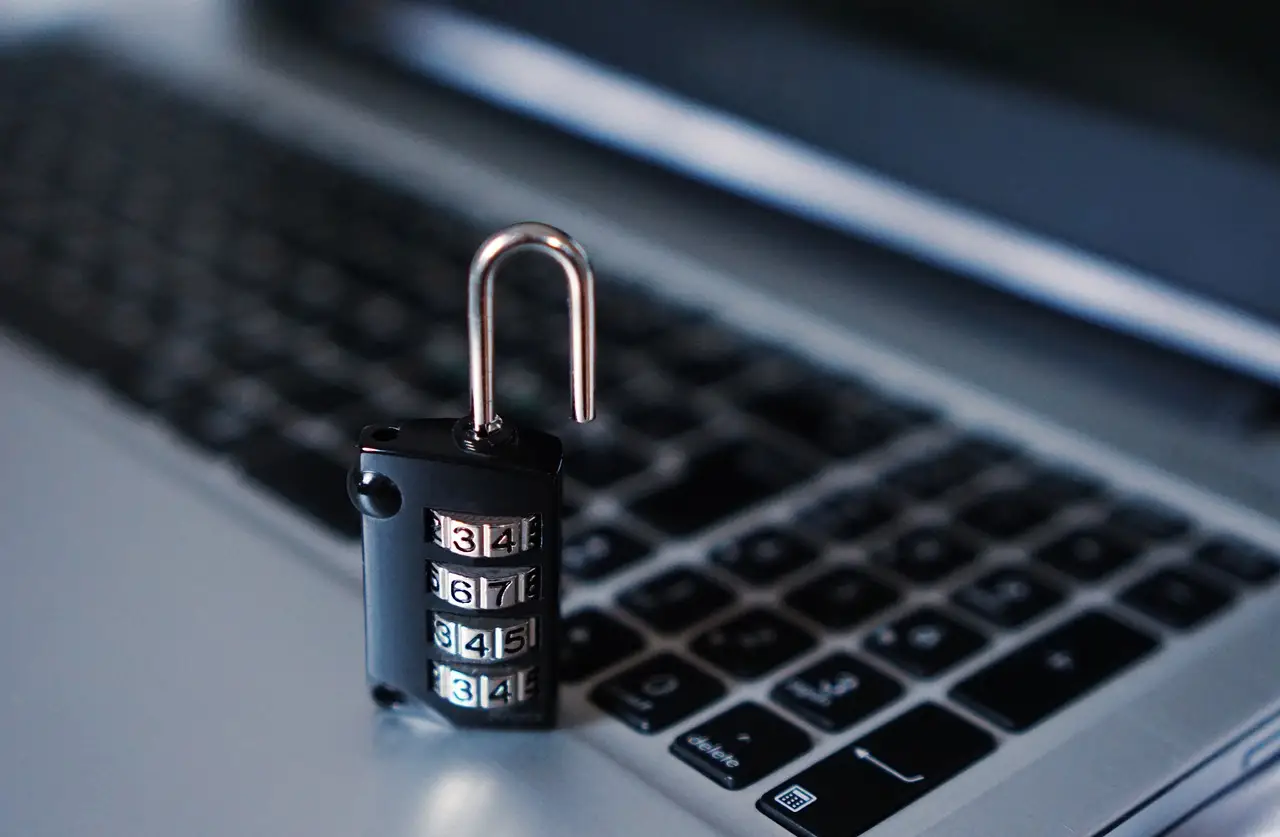 A black four-dial combination padlock, shackle open, standing on the keyboard of a silver laptop