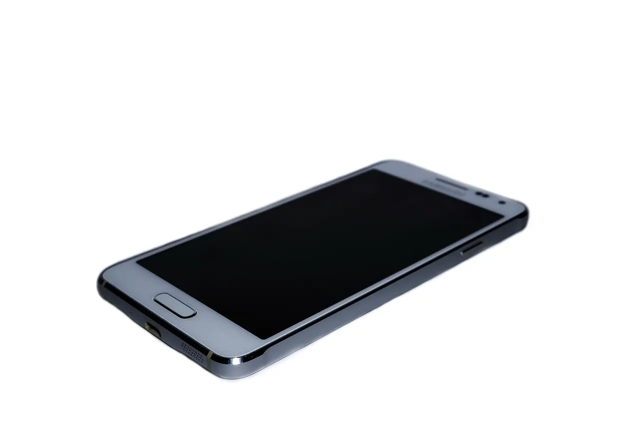 A silver Samsung Android phone with a blank screen lying on a white surface