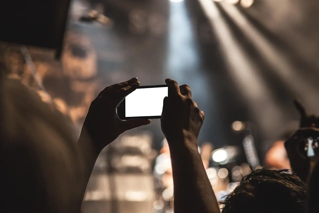 Two hands tilt a white-framed smartphone with a blank dark screen against a plain gray backdrop