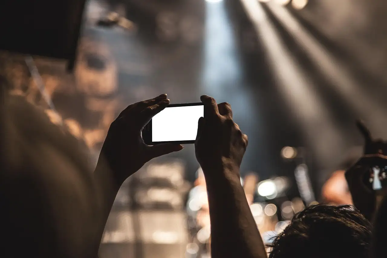 Two hands tilt a white-framed smartphone with a blank dark screen against a plain gray backdrop
