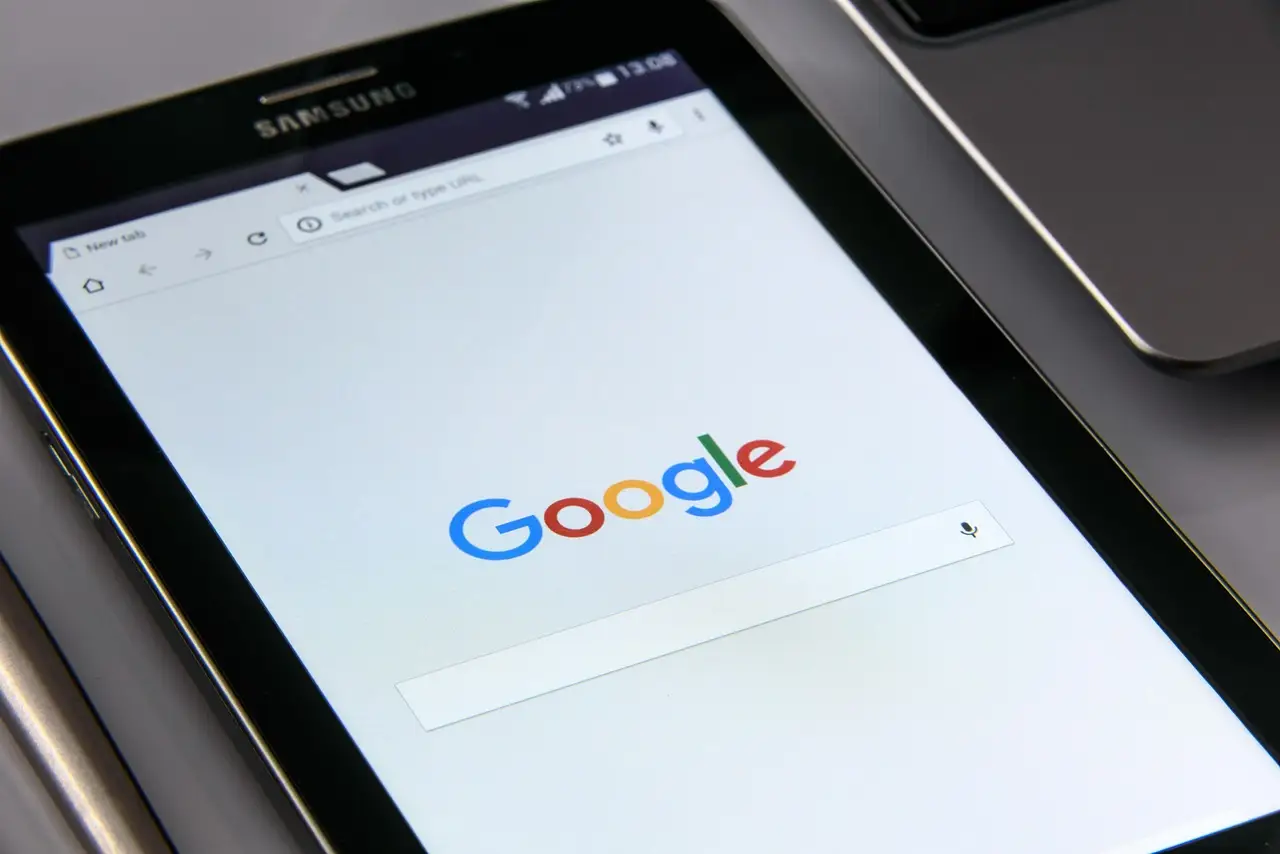 A Samsung Android device showing the Google search page in a browser, resting on a laptop