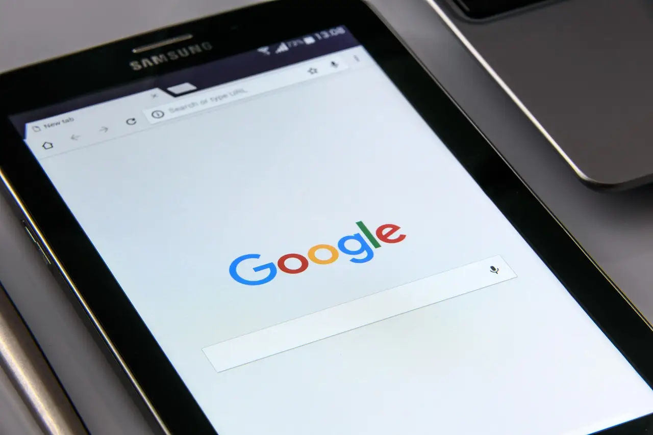 A Samsung Android device showing the Google search page in a browser, resting on a laptop