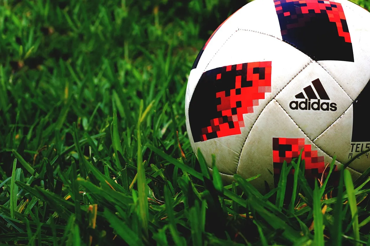 Adidas match ball with red-and-black pixel-print panels lying in long grass