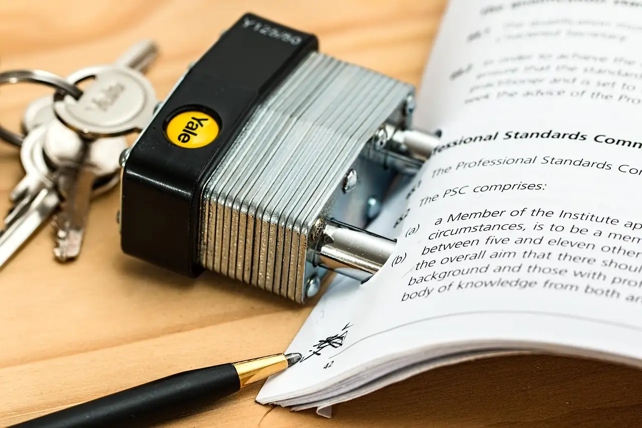 Yale padlock and keys resting beside an open printed document and a pen on a wooden desk