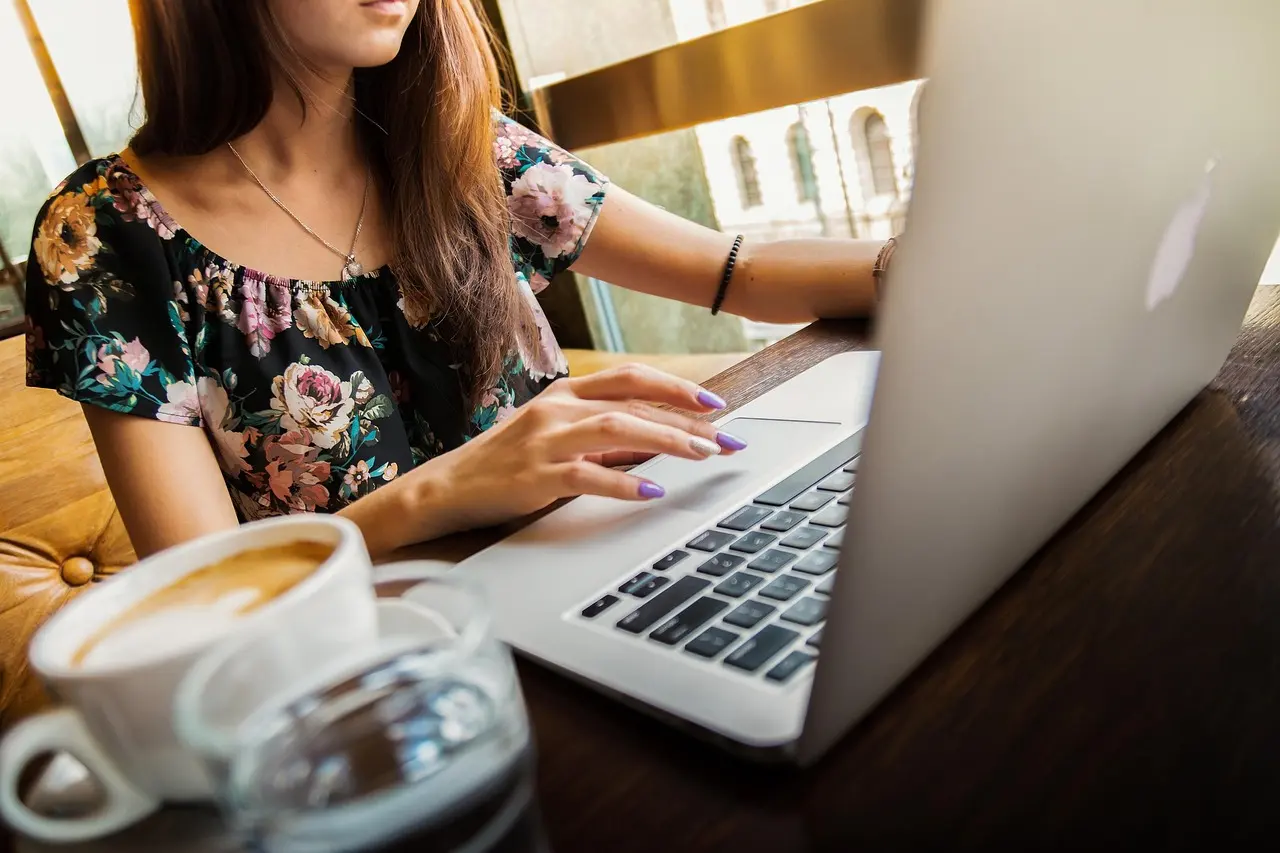 A woman typing on a laptop at a cafe table with a cup of coffee in front