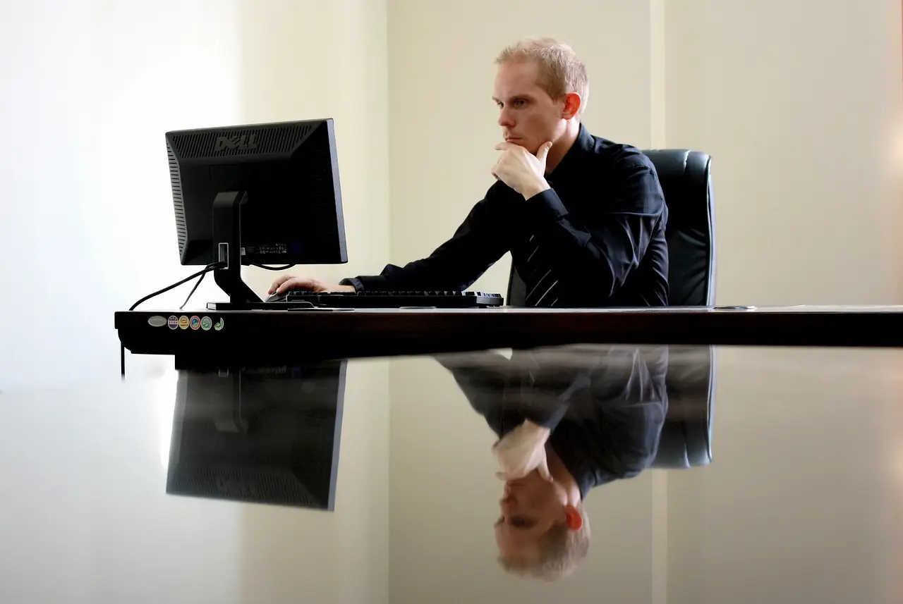 Apple desktop display showing a green mountain landscape wallpaper on a wooden desk with keyboard and mouse
