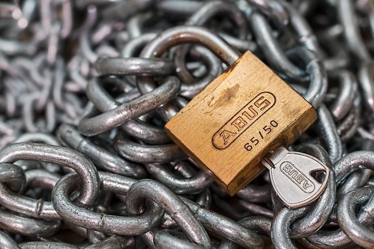 A brass padlock and its key resting on a heavy steel chain