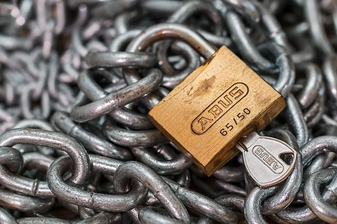 A brass padlock and its key resting on a heavy steel chain