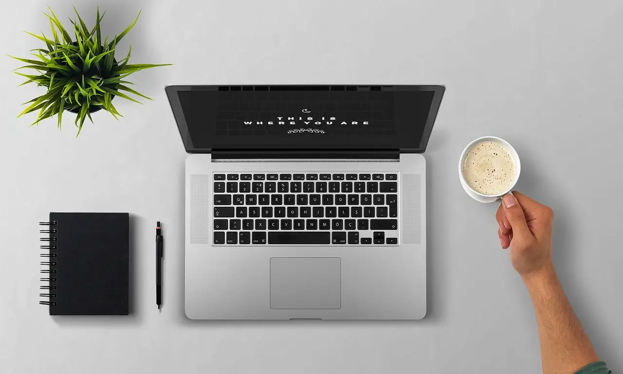 A laptop open on a desk with a cup of coffee.