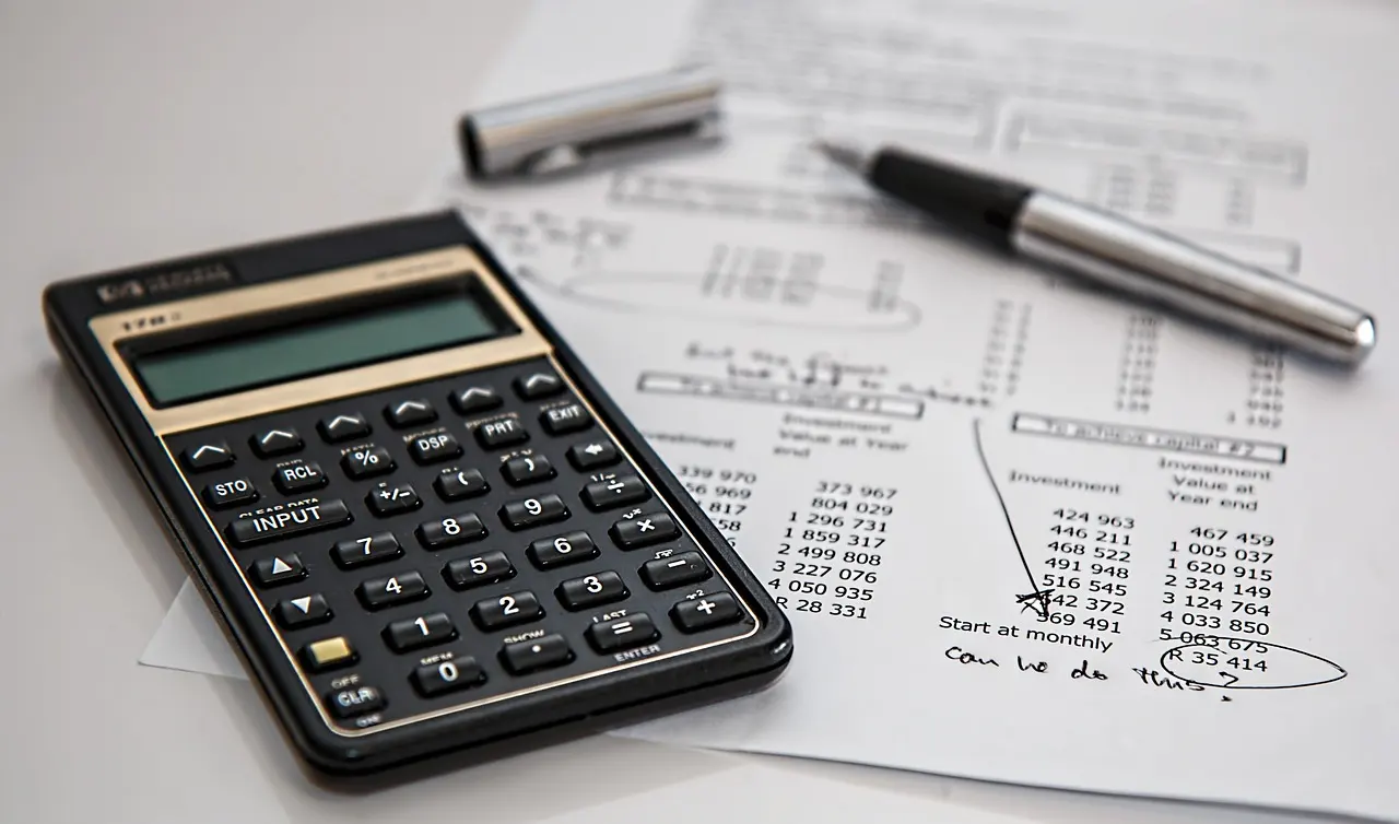 A calculator and pen resting on a printed financial spreadsheet full of numbers