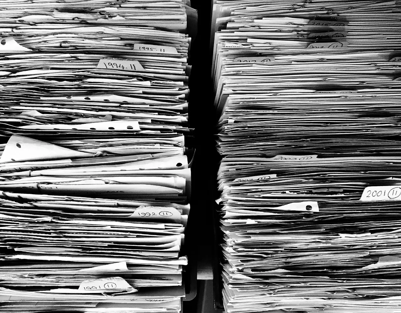 A stack of paper files and folders piled on a desk