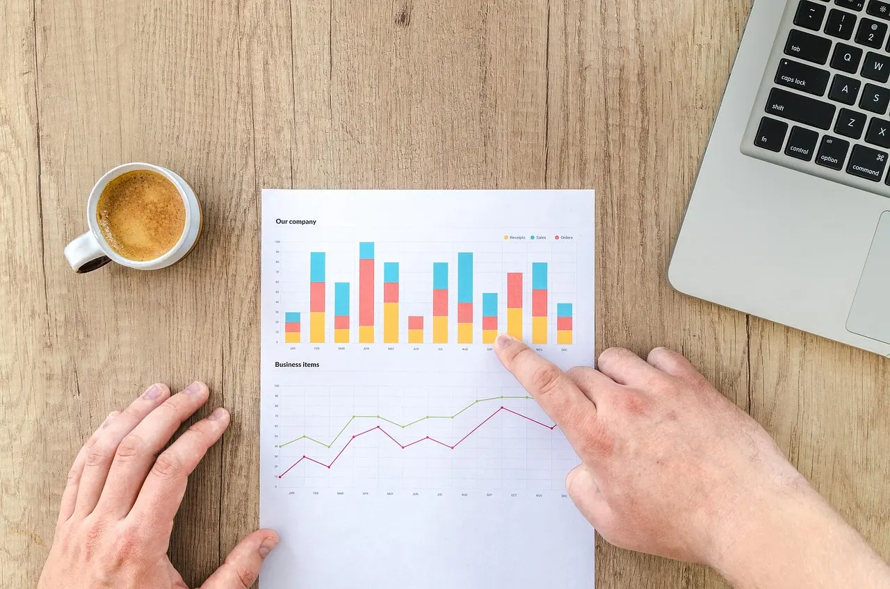 Hands pointing at printed business charts on a desk beside a coffee and a laptop