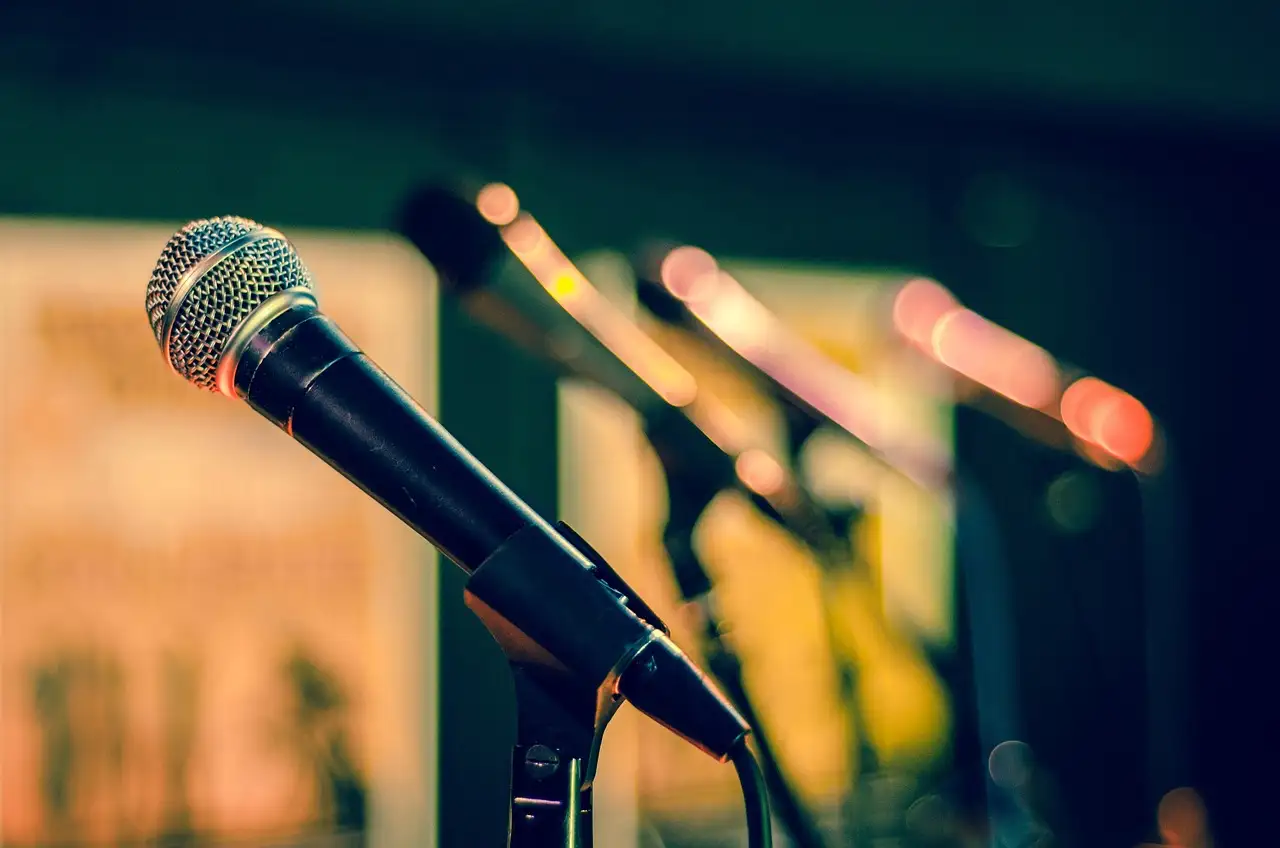Black handheld microphone on a stand in sharp focus, more mics blurred behind under warm stage lights