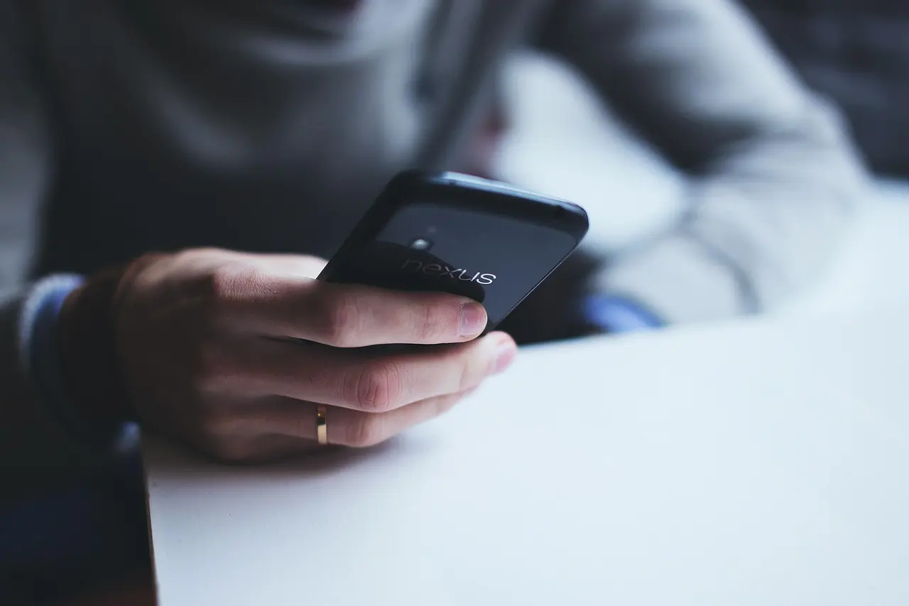 A person's hand holding a black Android phone over a white table