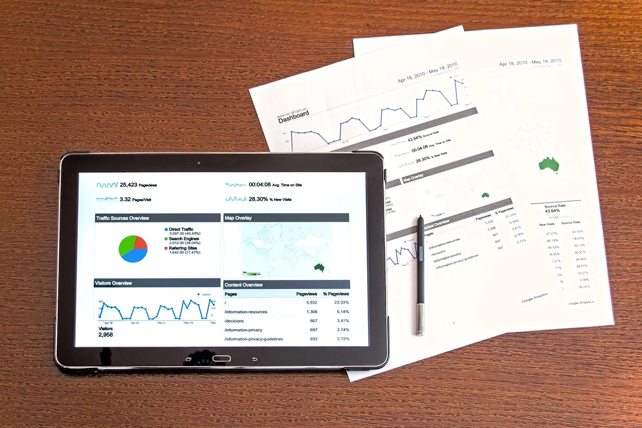 Tablet displaying a web analytics dashboard beside printed traffic reports and a stylus on a wooden desk