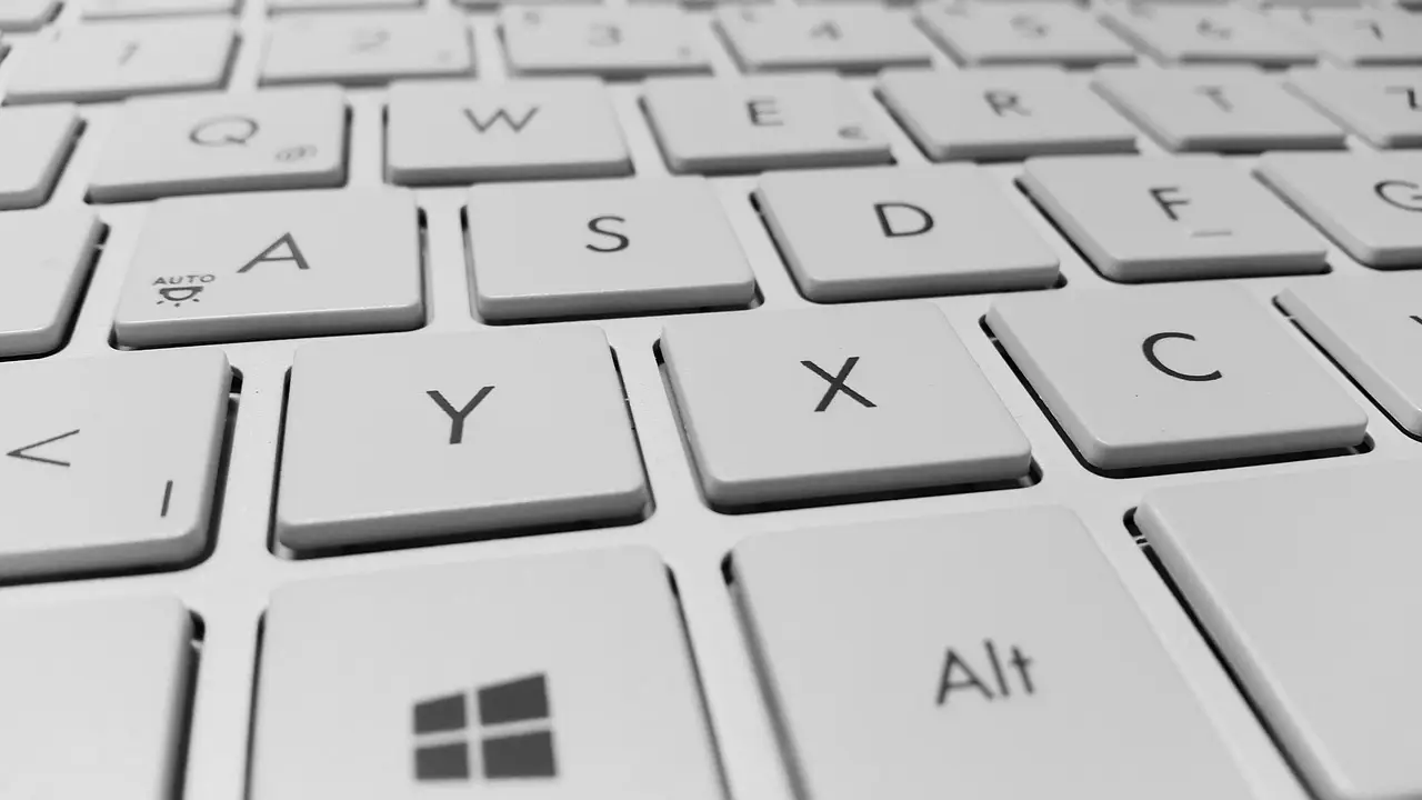 Man in a blue shirt writing on a small notepad beside an open silver laptop
