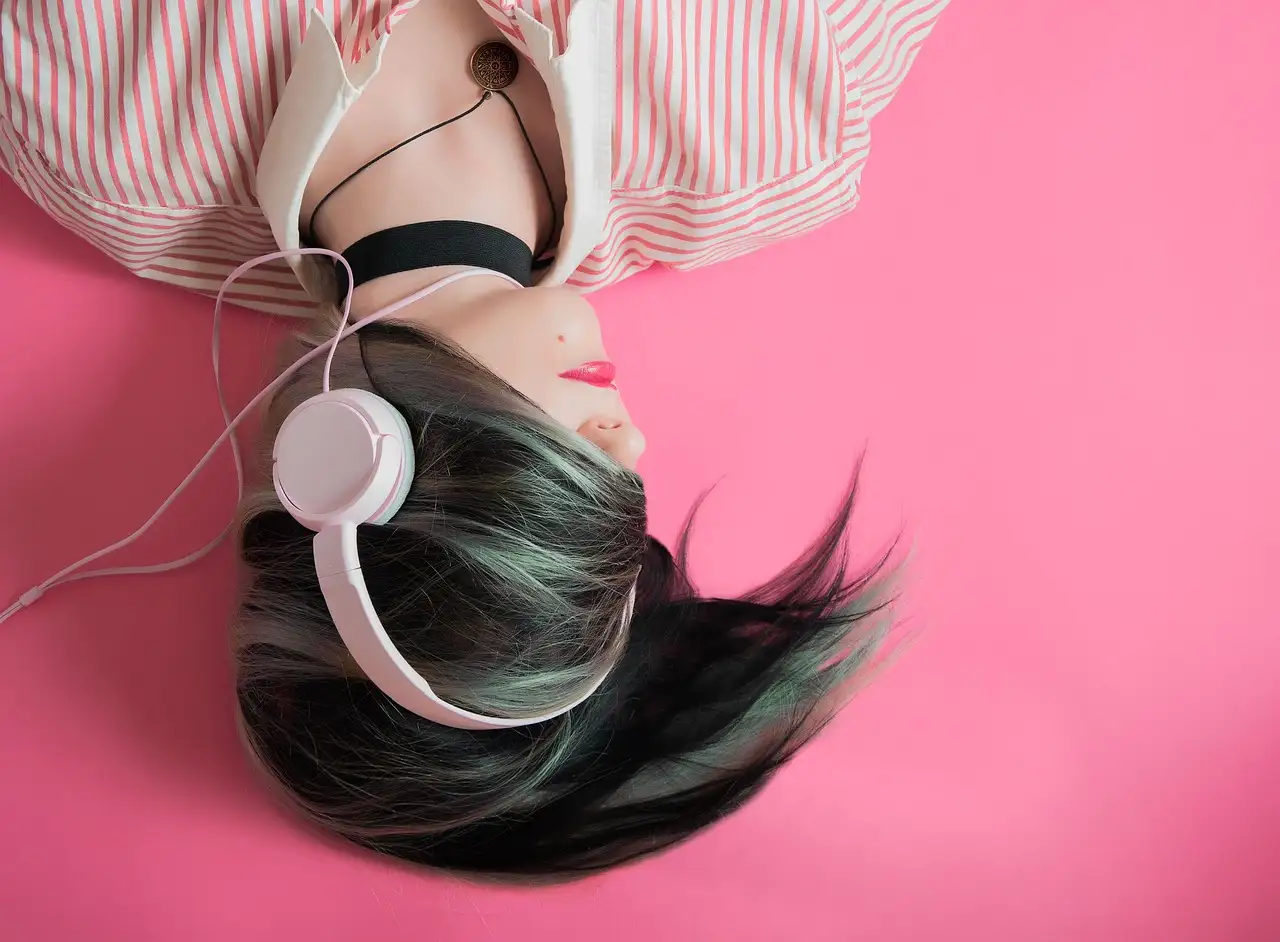 White Samsung earbuds coiled around a silver phone on dark wood, screen showing a Google Play headphone icon