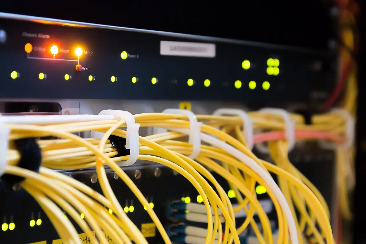 Bundles of yellow fiber cables run past a rack panel lit with green and orange status lights