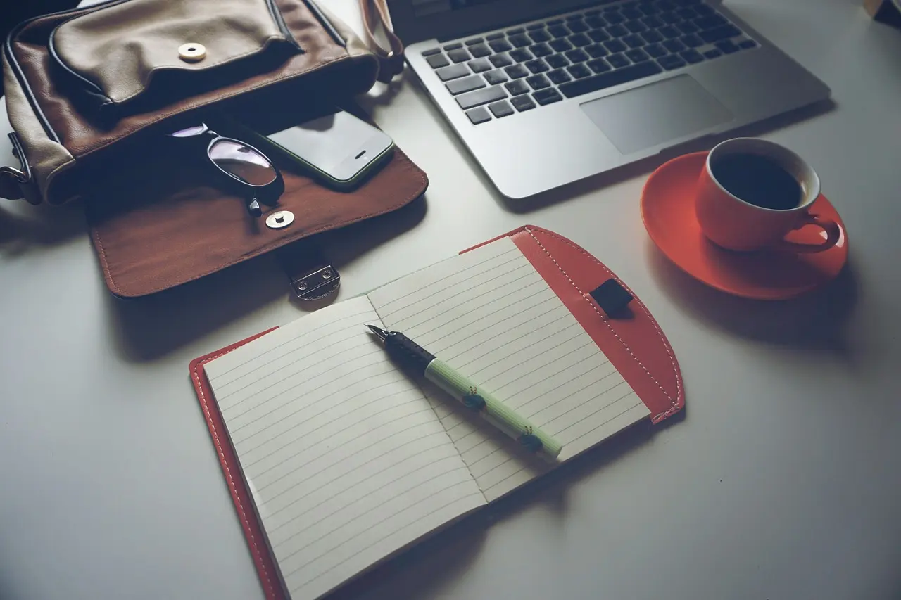 A laptop, notebook and coffee on a desk