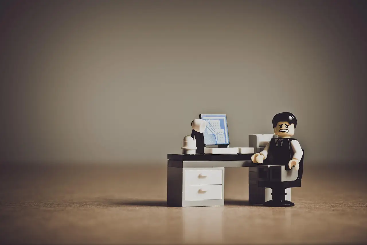 A frustrated person at a desk holding their head in their hands